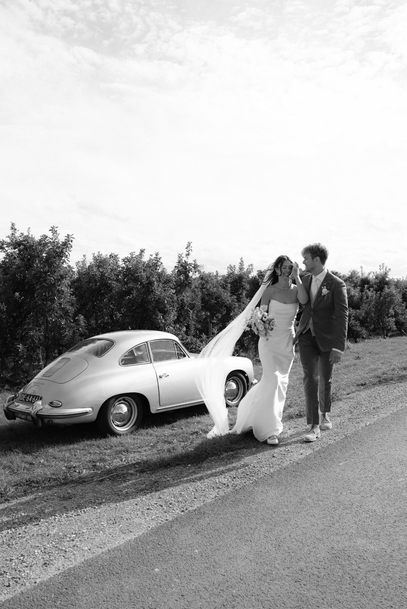 Black and white photo of a couple walking beside a vintage Porsche