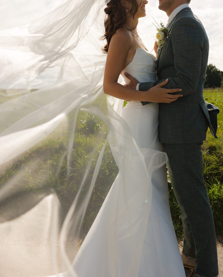 Couple embracing as the veil blows in the wind in a green field